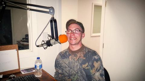 man in camo sitting in front of a mic in a studio